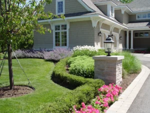 Driveway to a home with shrubs, flowers, and grasses