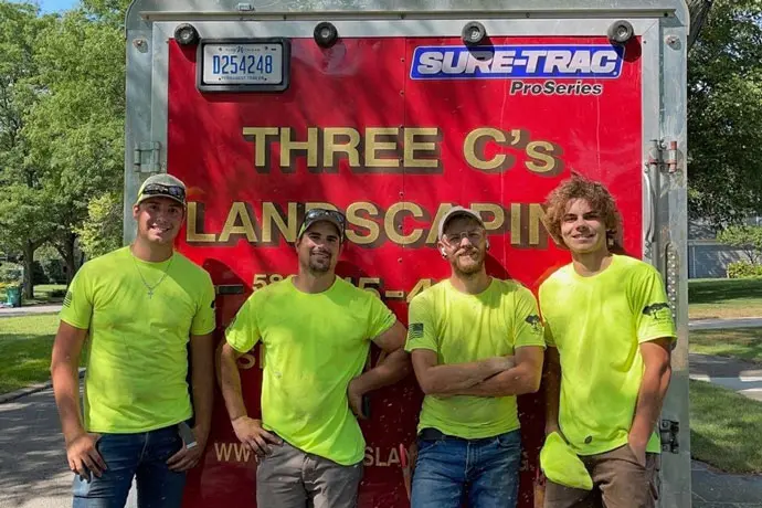 Four male Three C's Landscaping employees smiling in front of truck